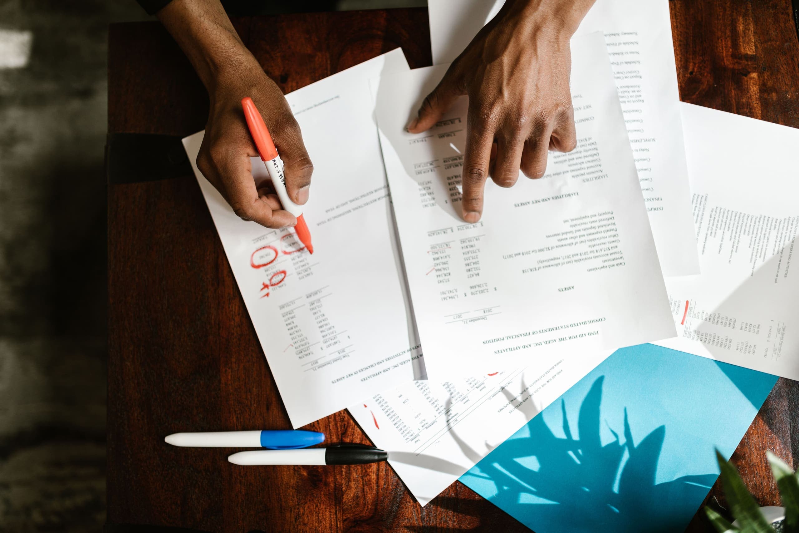 Hands marking up paper documents on a desk
