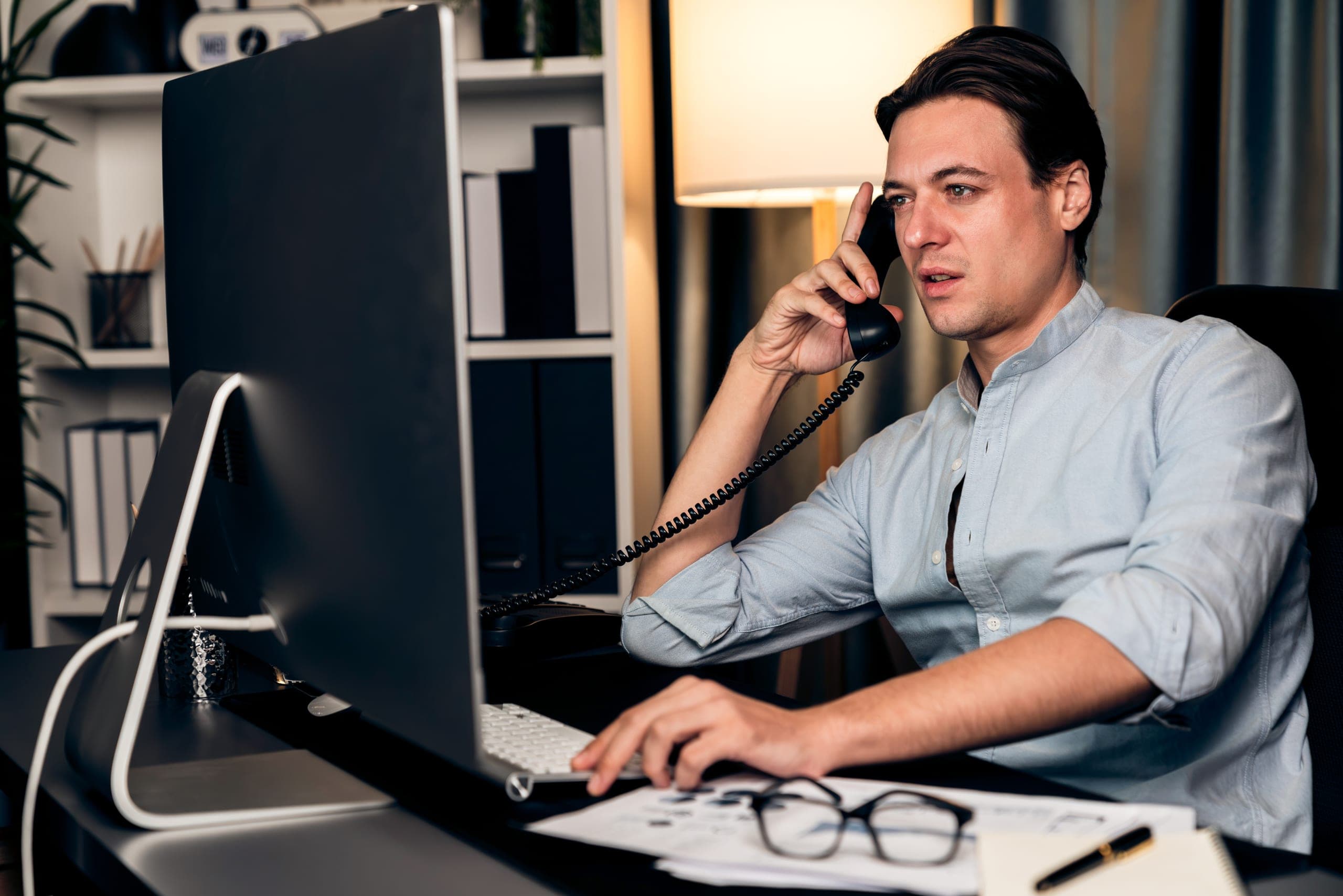 Man on a desk phone at his computer